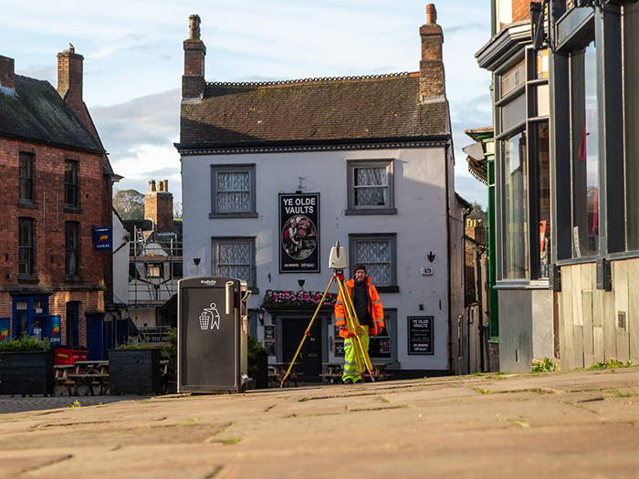 A male Derbyshire county council employee in hi-vis clothing stands by a scanner on a tripod in Ashbourne Market Place